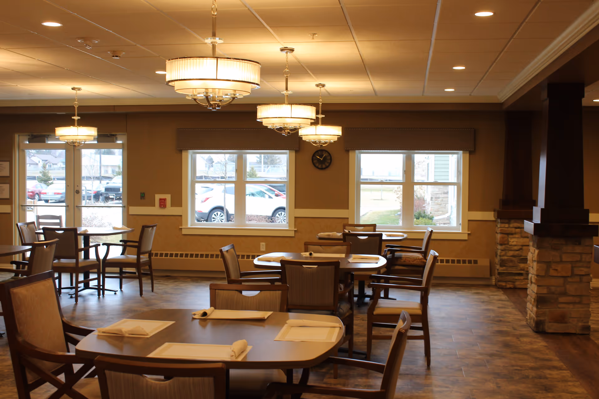 Dining room with multiple set tables and chairs, pendant lights, windows, and a stone pillar.