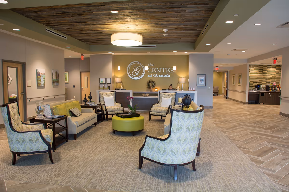 Lobby of The Center at Grande showing arranged seating, a round green ottoman, and the reception desk with the facility sign on the back wall.