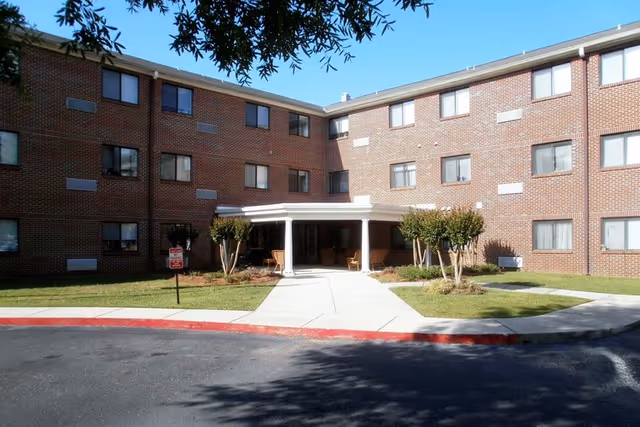 Brick senior apartment building exterior with a covered entrance and landscaped front yard.