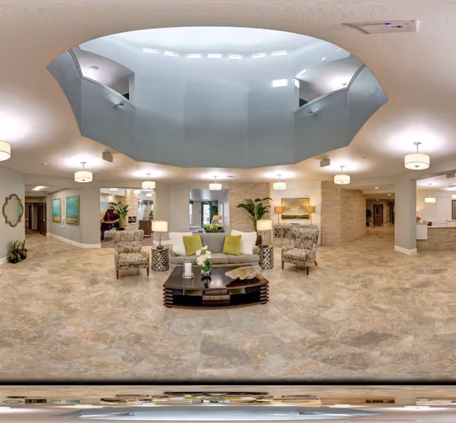 Bright, spacious senior living lobby with a central seating area, coffee table, plants, and a large circular skylight.