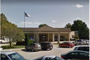 Sunrise Hill Care & Rehab Center's front entrance with a porte-cochere, parked cars, and a flag.