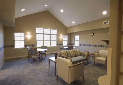 A cozy lounge with couches, chairs, and tables in a sunlit senior living hall.
