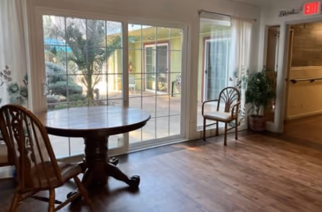 Wooden table and chairs in a bright common room with large sliding glass doors opening to a courtyard.