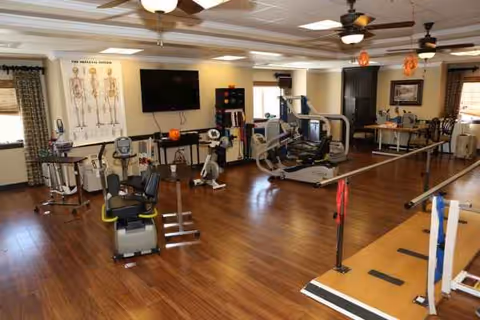 A spacious interior rehabilitation gym with cardio machines, weights, and benches.
