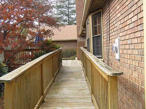 Outdoor wooden ramp along a brick building with railings and trees nearby.