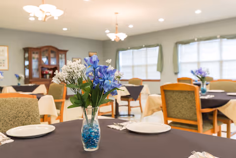 Dining room with tables set for a meal, each topped with a vase of blue and white flowers.