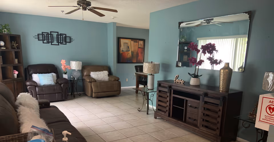 A teal-walled living room with tile floors containing leather recliners and a sofa, a wooden media console with a large mirror and decorative items, lamps, and wall art.