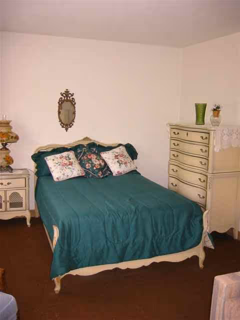 A vintage bedroom with teal bedspread, floral pillows, and cream furniture.