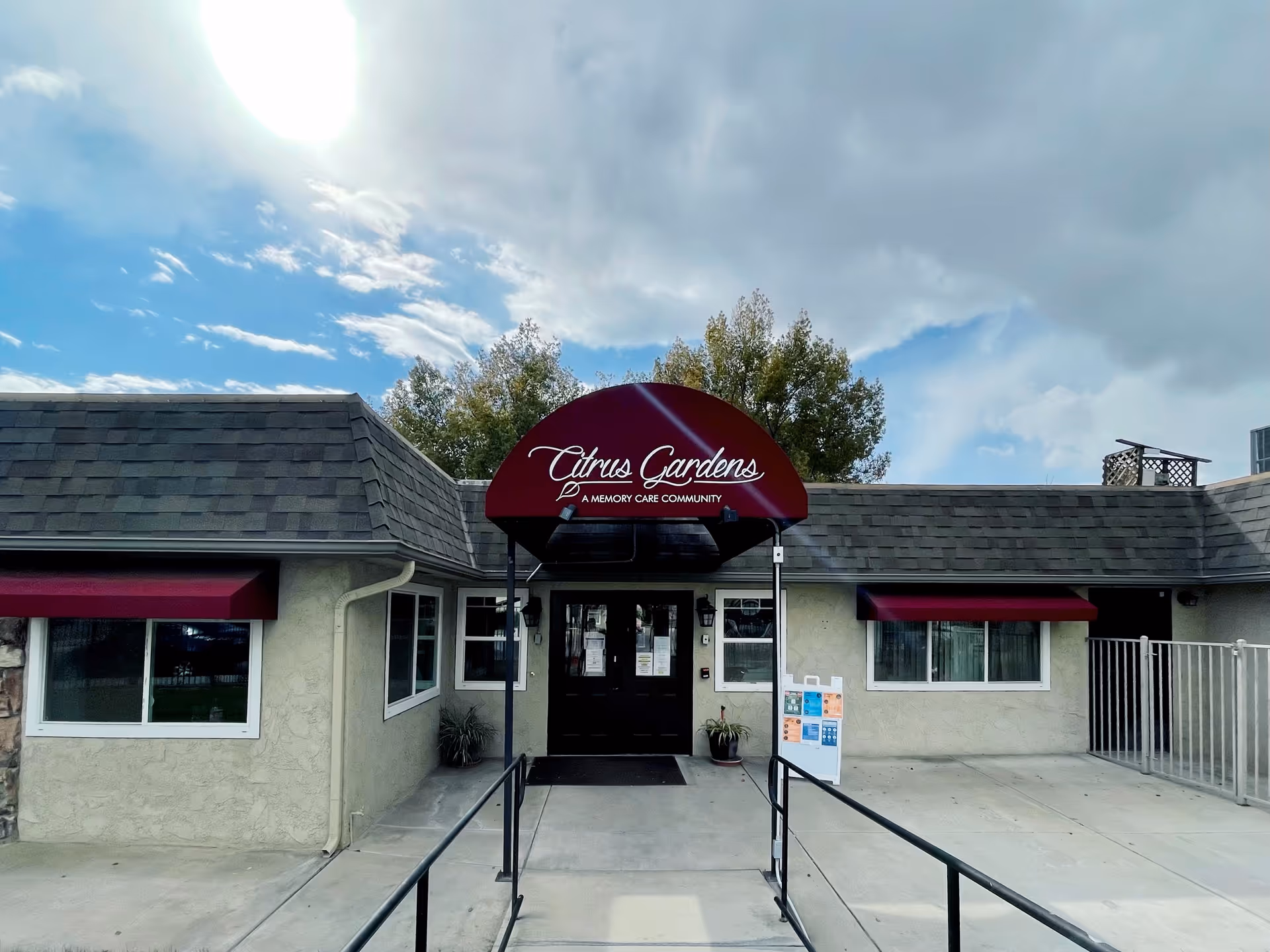 Front entrance of Citrus Gardens Memory Care Community with maroon sign canopy and ramp.