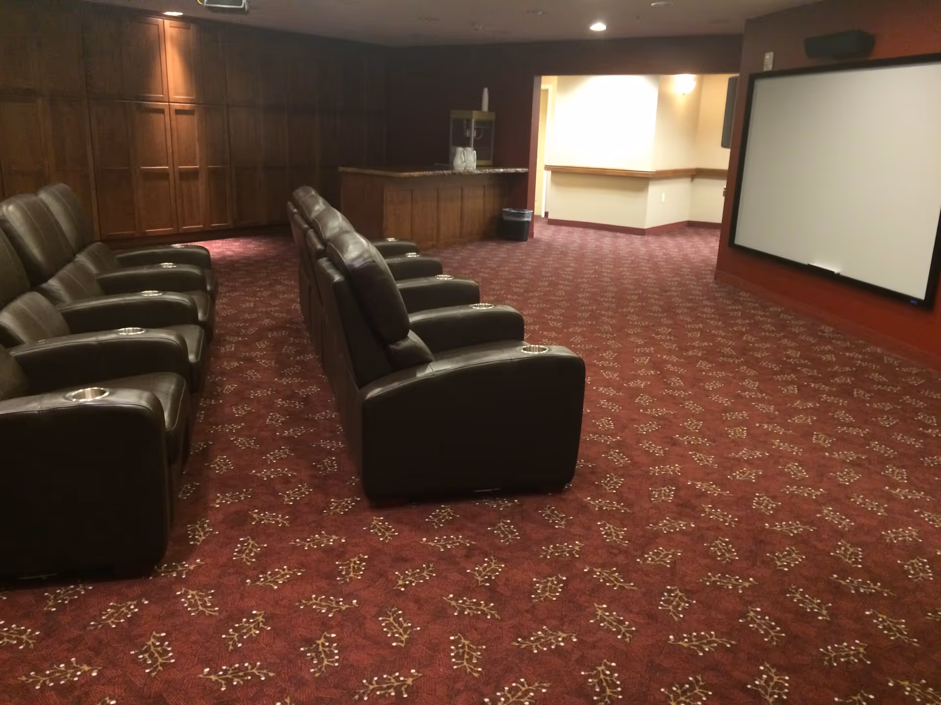 Small screening room with rows of leather recliner seats facing a projection screen and a concession counter at the back.