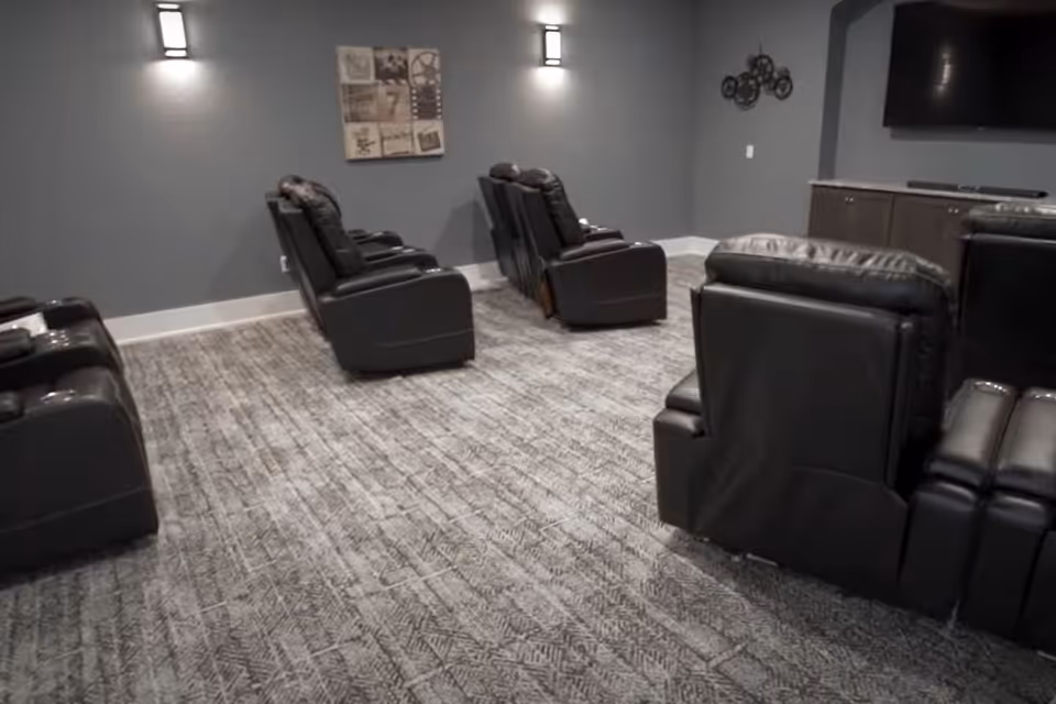 A small theater-style room with rows of black leather recliner chairs facing a wall-mounted TV.