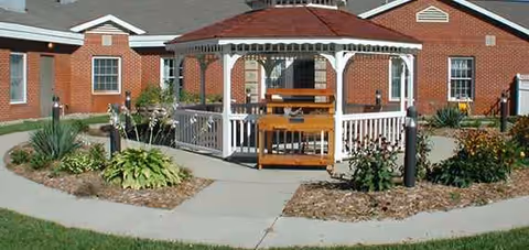 Exterior of Maple Lawn facility with white gazebo, paved path, and landscaped garden beds.