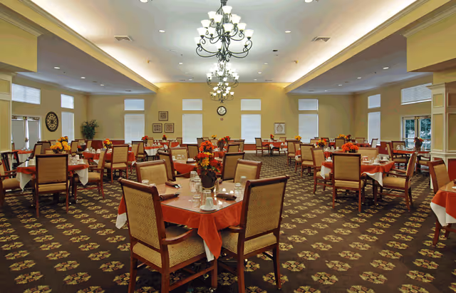 Large dining room with numerous tables set with red tablecloths, floral centerpieces, and chandeliers.