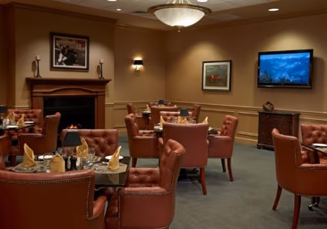 Cozy dining room with tufted leather chairs, set tables, a fireplace and a wall-mounted TV.