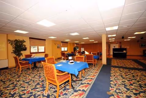 Empty senior living dining area with blue tablecloths and patterned carpet.
