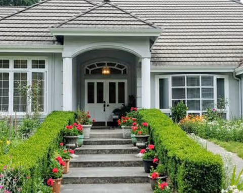 Front entrance of a senior care facility with stairs, hedges, and potted flowers.