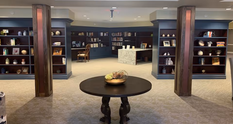 Spacious interior common area with a round table in the foreground and built-in bookshelves and seating along the walls.