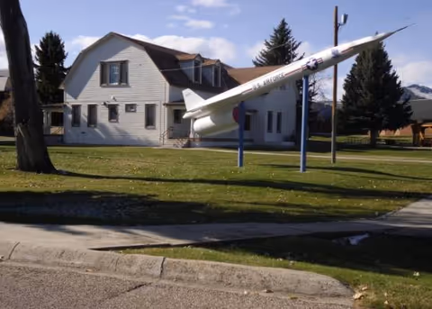 White two-story building with a rocket sculpture on a grassy lawn in front.