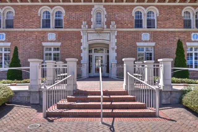 Brick building front with a central arched entrance accessed by steps and metal handrails.