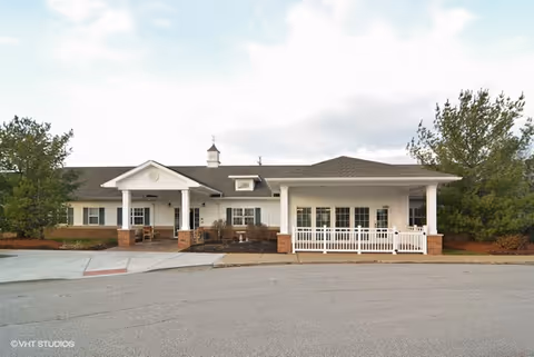 White, single-story senior living facility with columns, a brick porch, and a driveway.
