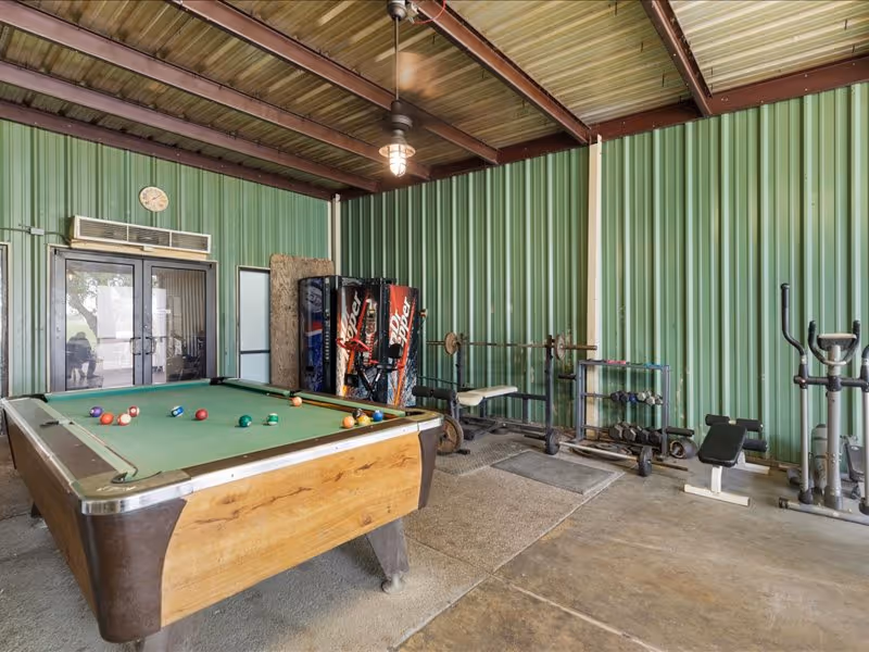 Indoor recreation room with a pool table, vending machines, and exercise equipment against green metal walls.