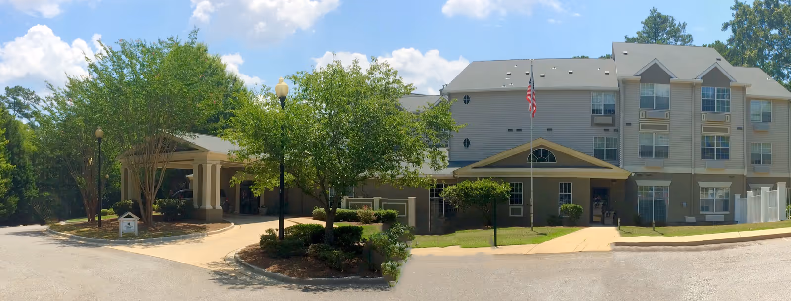 Front exterior of The Landings of Columbus senior living building with a covered entrance, flagpole, and landscaped driveway.