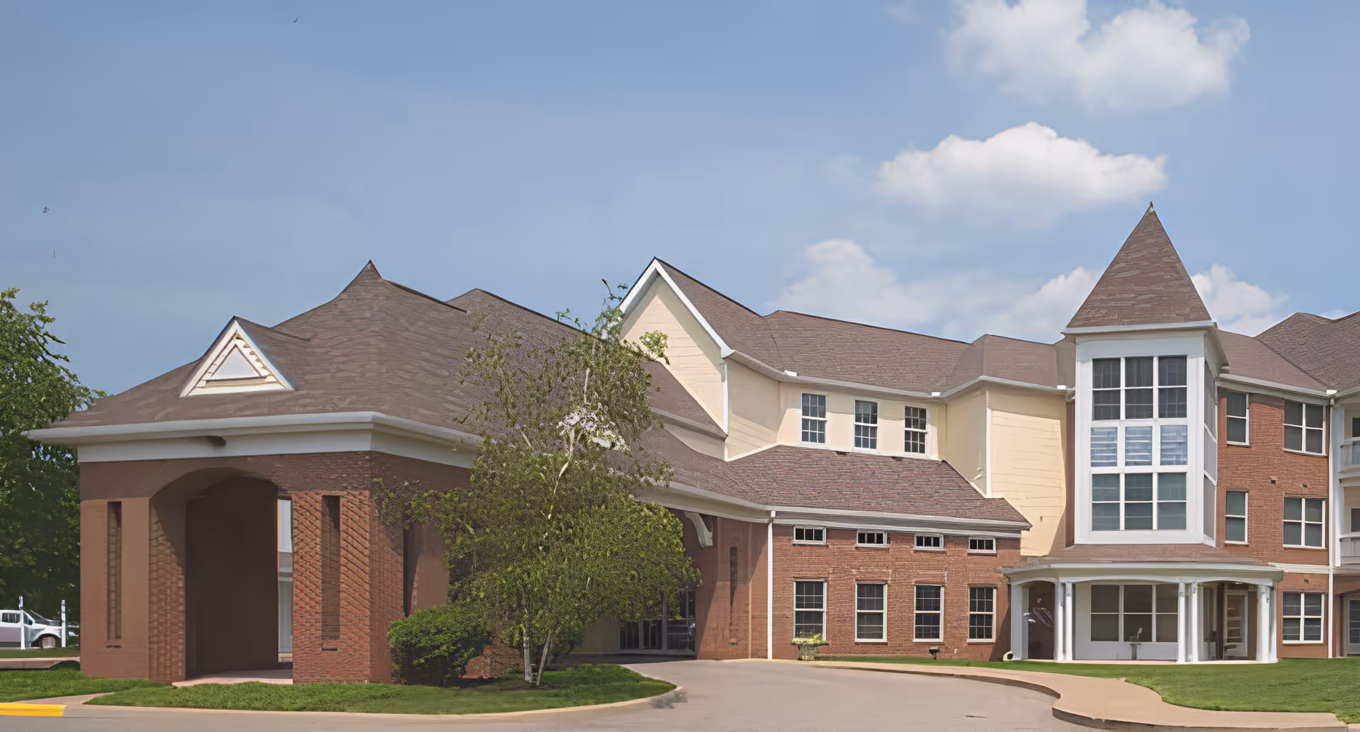 Front exterior of a multi-story brick senior living building with a covered porte-cochère and a large windowed tower.
