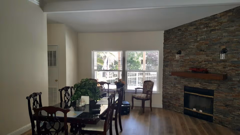Dining area with a dark wood table and chairs near windows and a stone fireplace wall.