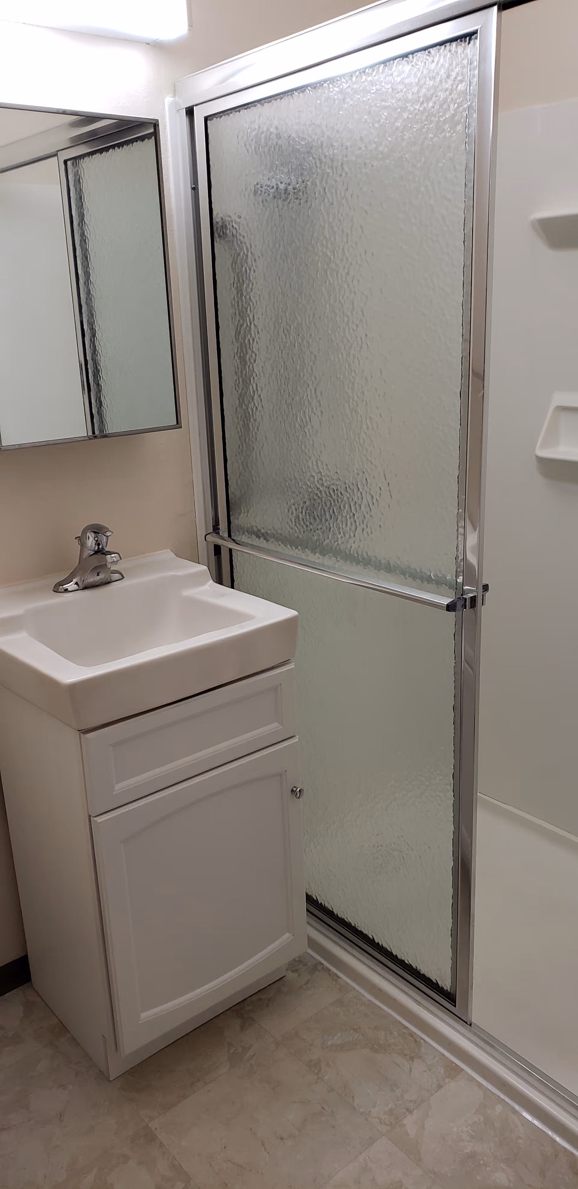 Small bathroom with a white sink vanity, mirrored medicine cabinet, and a frosted glass sliding shower door.