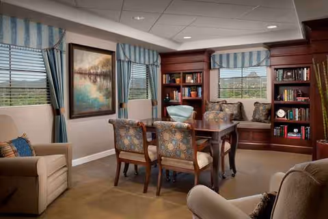 Cozy senior living common room with a wooden dining table, chairs, and blue-striped curtains.