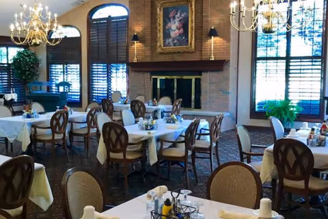 A formal dining room with chandeliers, a brick fireplace, and round tables set with white linens.