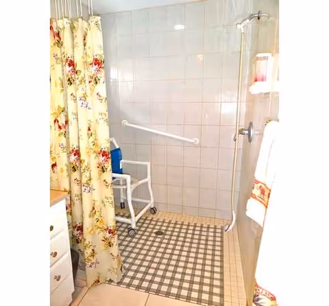 Bright senior living bathroom with a shower chair, grab bar, and floral curtain.