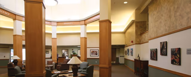 Spacious retirement community lobby with tall wooden columns, seating areas, and artwork on the walls.