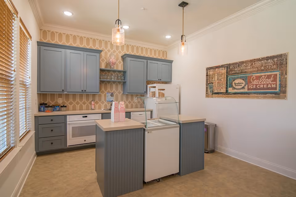 Small kitchenette with blue-gray cabinets, an island holding a glass display freezer, pendant lights, and a vintage ice cream sign on the wall.