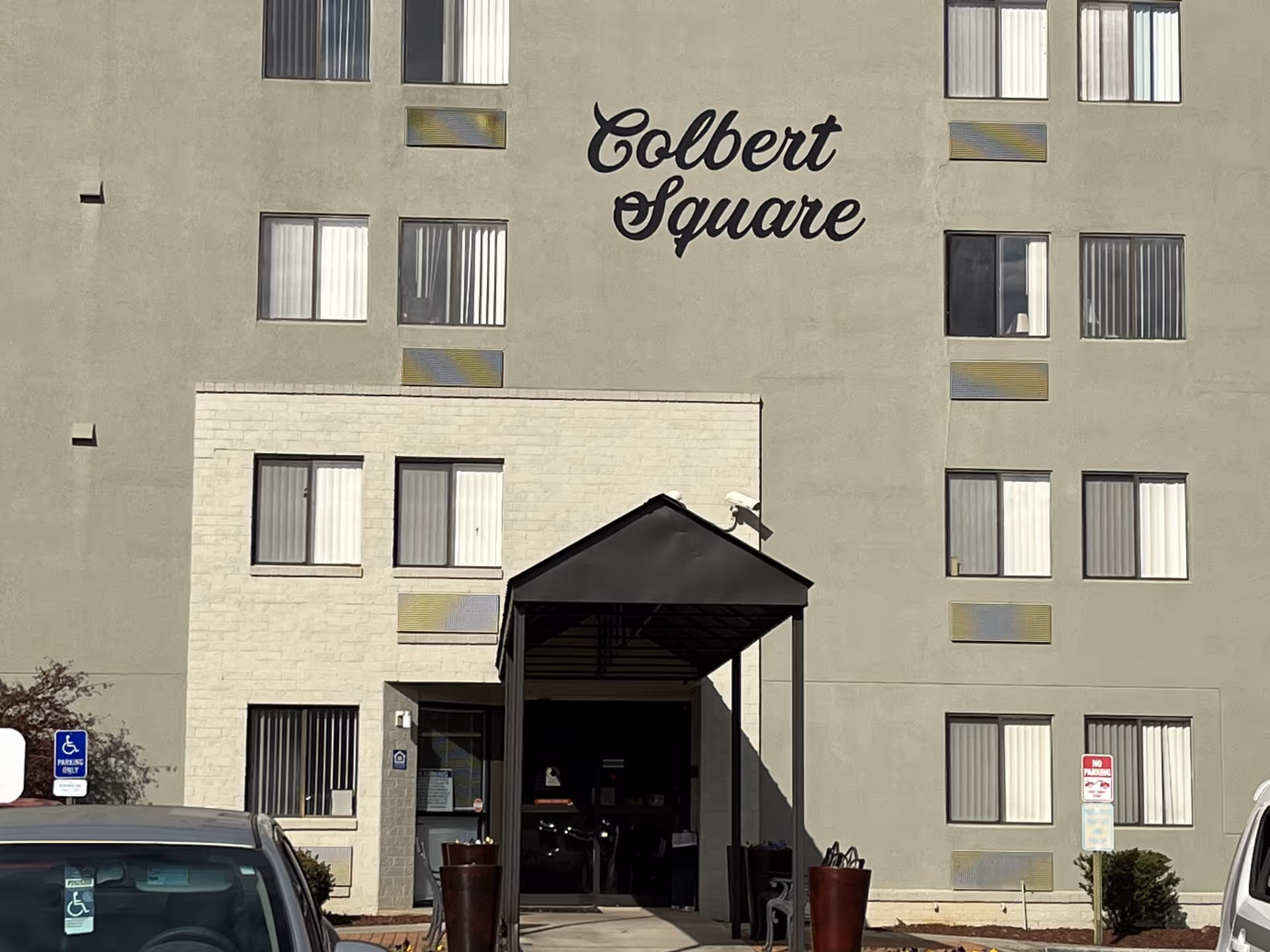 Front exterior of a multi-story senior housing building with a canopy entrance and 'Colbert Square' signage on the facade.
