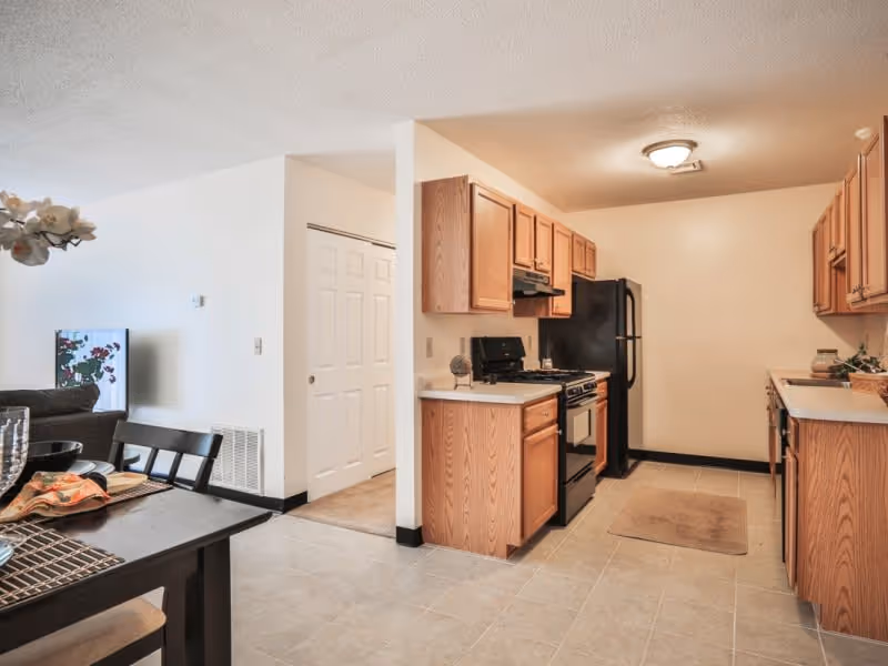 Open kitchen with oak cabinets, black appliances and an adjacent dining area and living space.