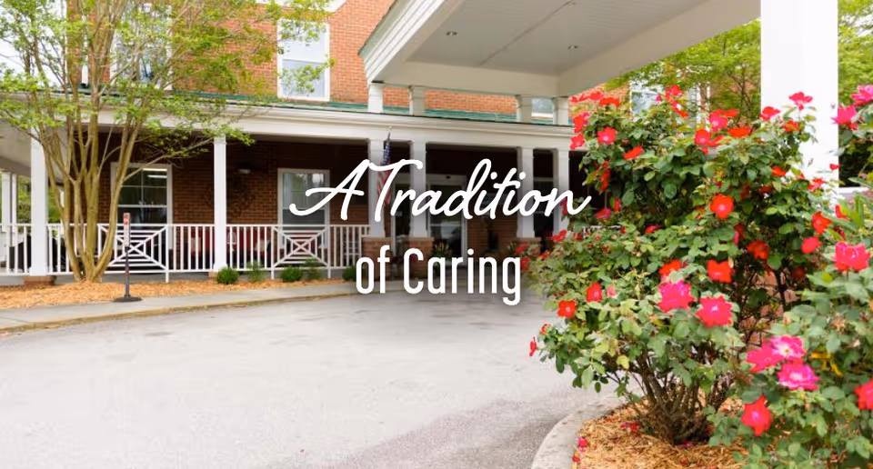 Front entrance of a brick building with a covered portico, driveway and blooming pink flowers.