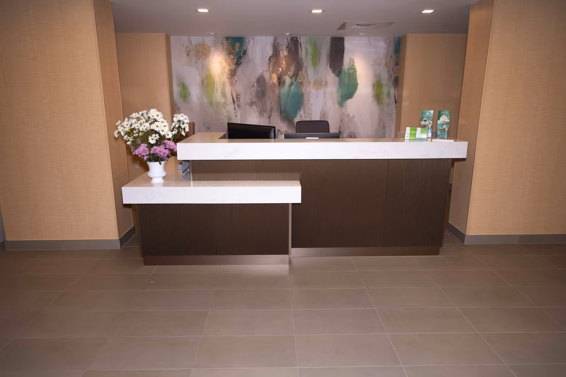 Reception desk in a healthcare facility with a white countertop, vase of flowers, and abstract artwork on the back wall.