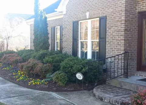 Brick care home exterior with manicured shrubs, a curved concrete path, and steps.