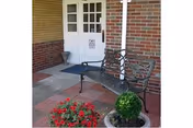 Entrance to a brick building with a white paneled door, a bench, potted plants, and a small welcome mat.