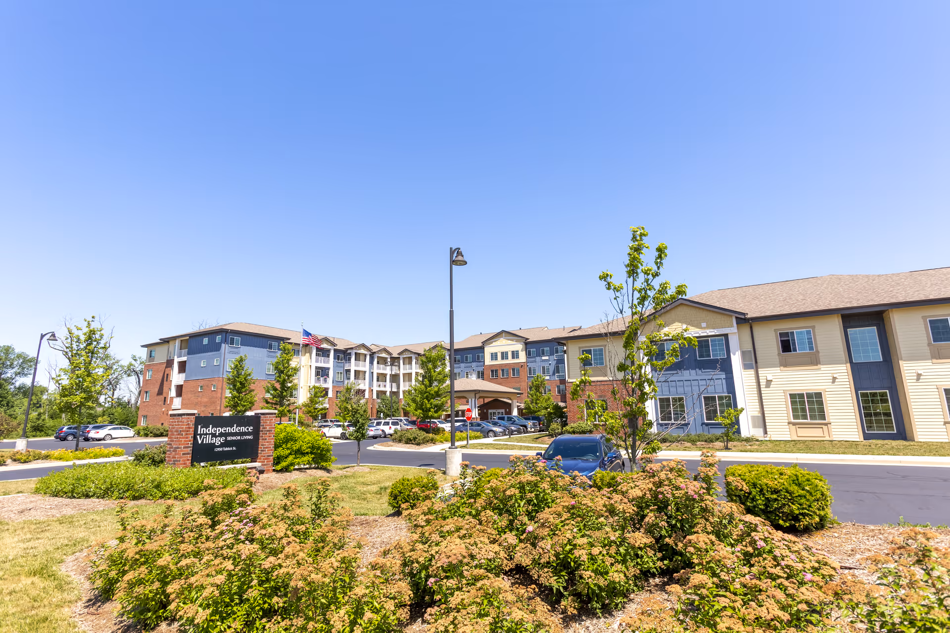 Exterior front view of Independence Village senior living building with landscaped grounds, driveway, and entrance sign.
