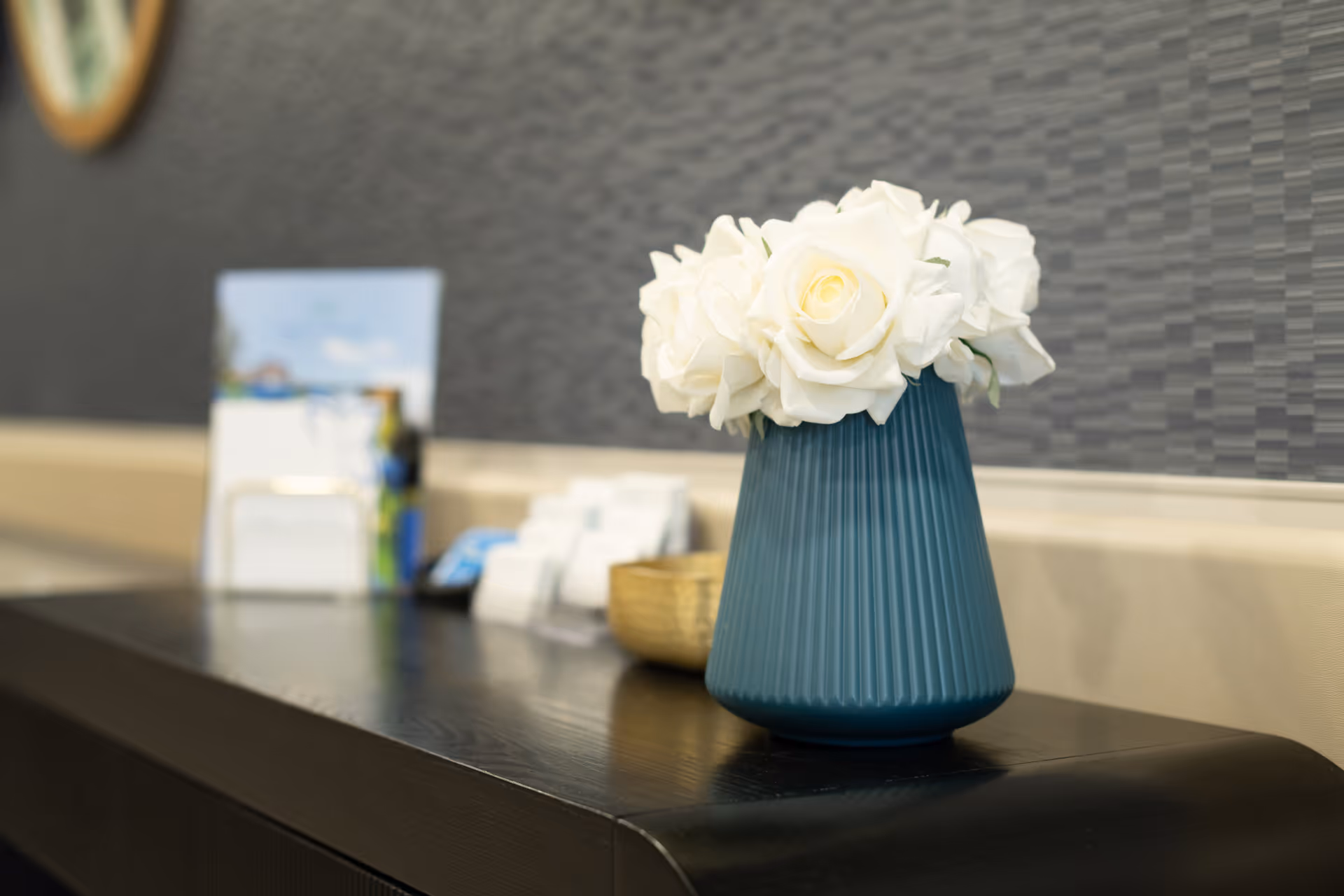 Teal vase holding white roses on a dark countertop in front of a textured gray wall.