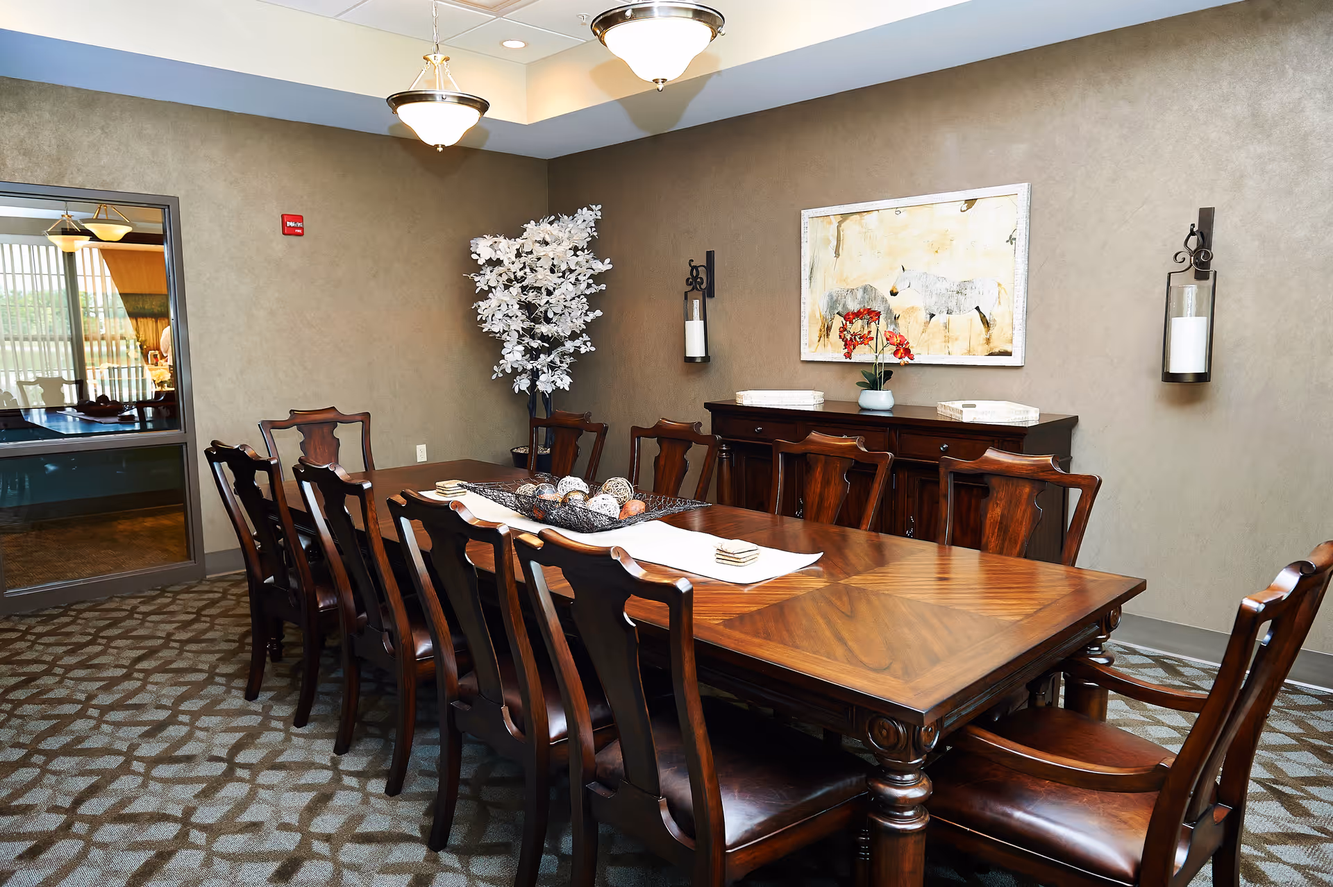 A formal dining room with a long wooden table surrounded by chairs, wall art, and decorative accents.