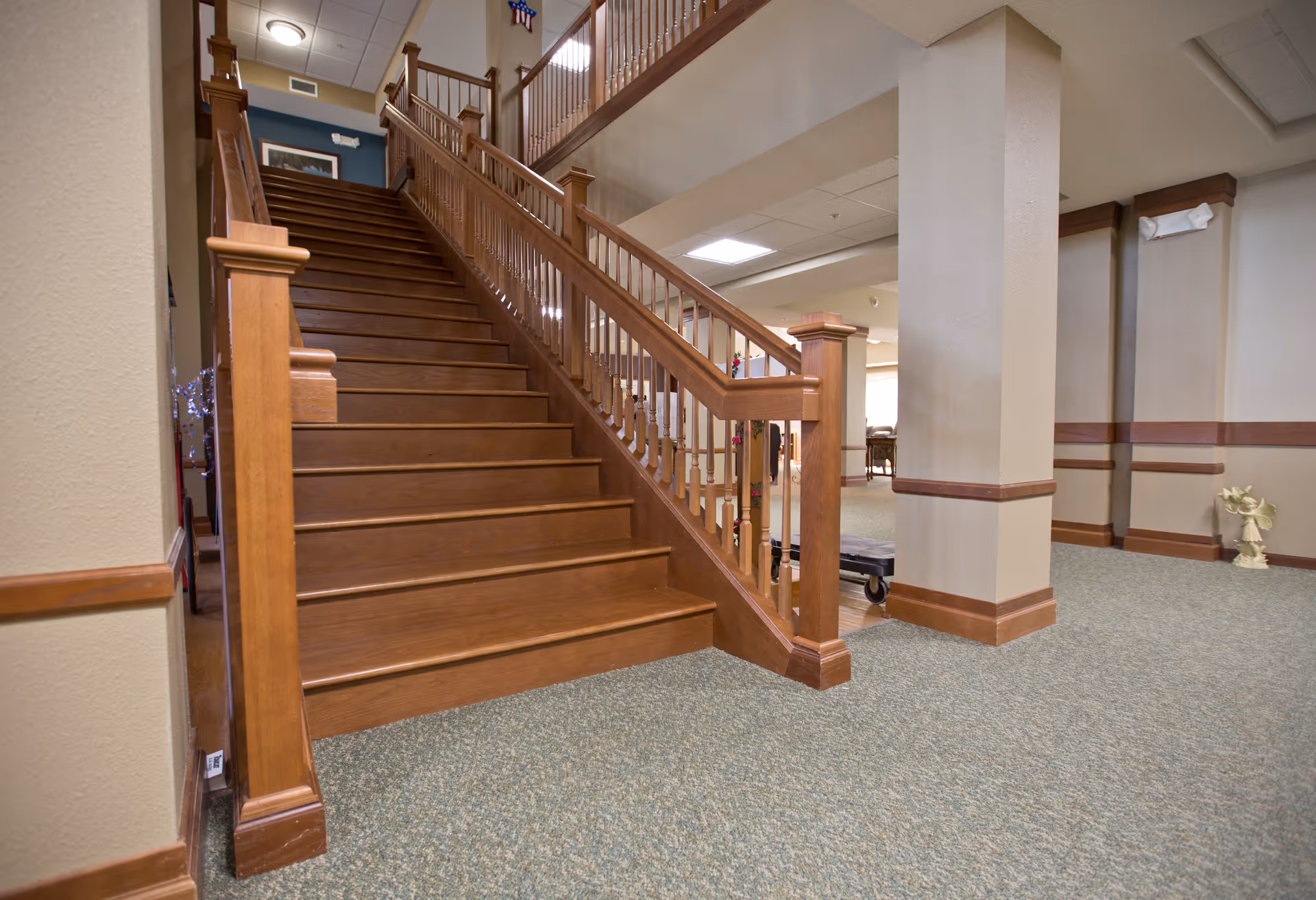 Carpeted interior lobby featuring a wide wooden staircase with a handrail leading to an upper level.
