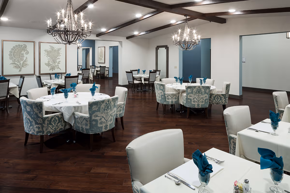 Elegant dining room with round tables, upholstered chairs, chandeliers and place settings.