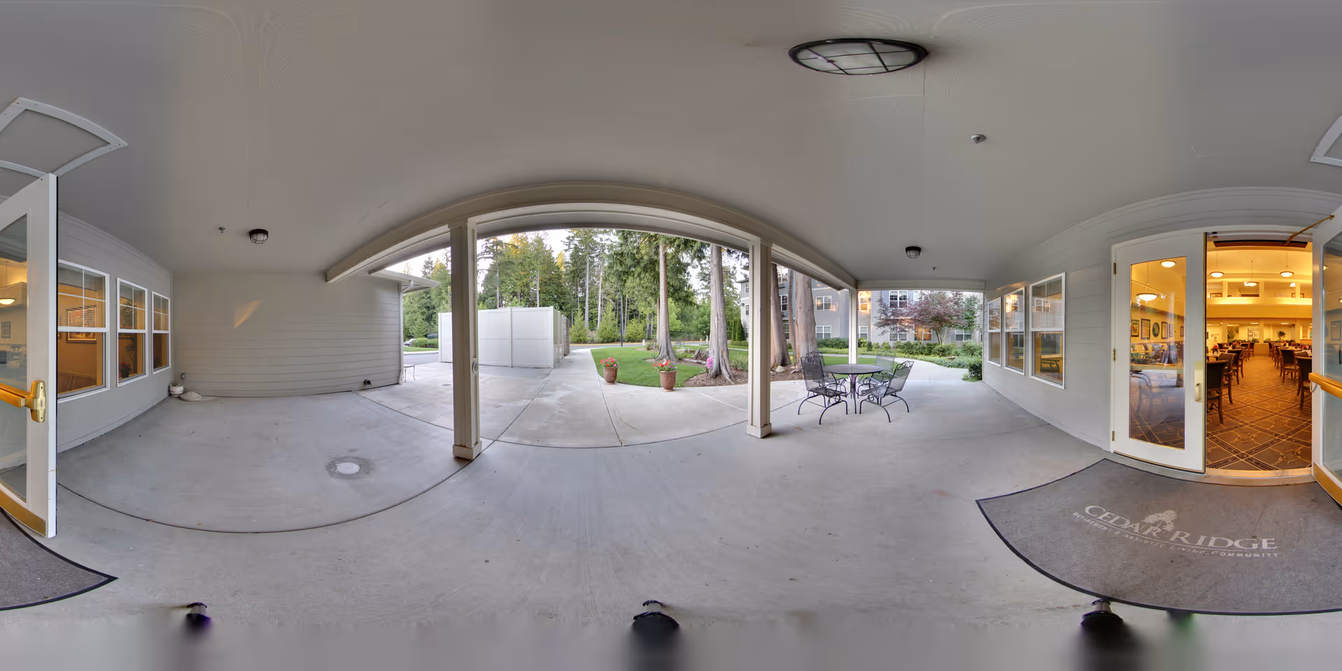 Covered outdoor entrance patio with seating and columns leading to a garden and the Cedar Ridge building entrance.