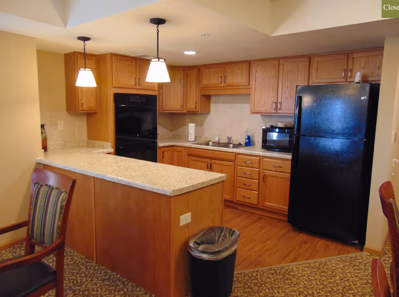 Kitchen area with a granite-topped island, wooden cabinets, a black refrigerator and oven, sink and pendant lights.