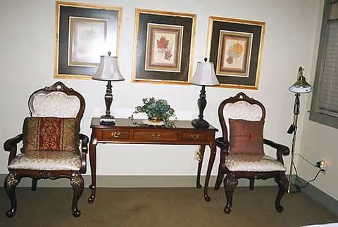 Two ornate chairs flank a wooden console table with lamps and framed artwork.