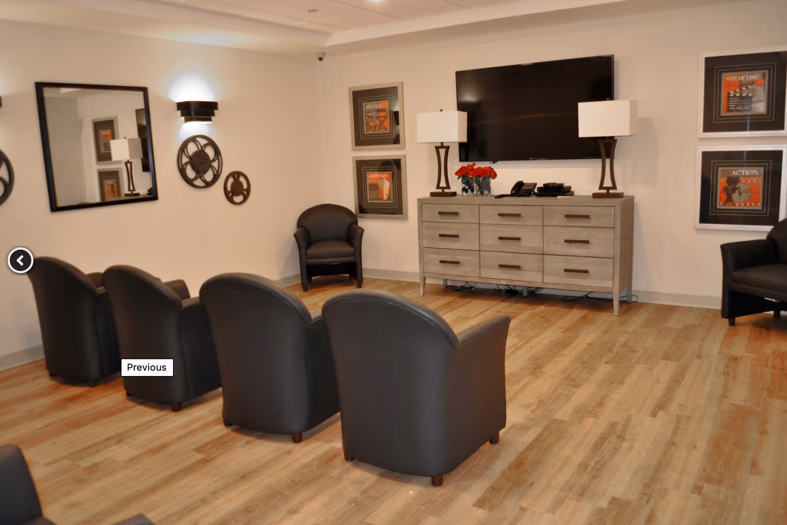 A cozy media lounge with rows of leather chairs facing a wall-mounted TV above a wooden console and framed artwork.