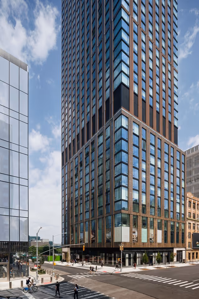Tall modern high-rise with a glass and brown facade at a city street intersection.